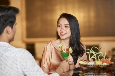 Otelde tanınmayan bir adamın önünde oturan ve gülümseyen çekici genç bir kadının omzunun üstünden çekilen fotoğrafı.