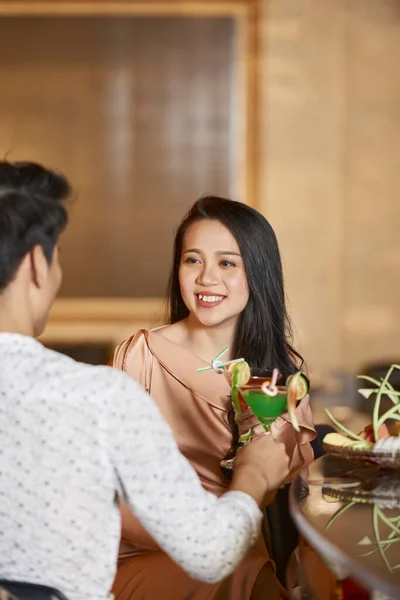 Over-the-shoulder shot of young woman sitting in front of unrecognizable man in hotel saloon smiling