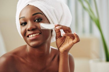 Yeni göz altı bandı takmış, gülümseyen siyah bir kadının yatay yakın portresi.