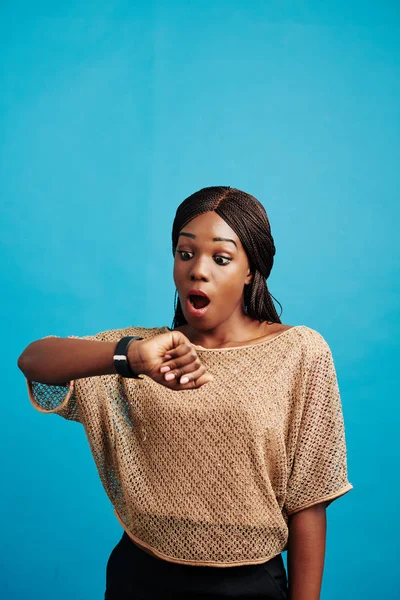 Vertical studio portrait of Black woman getting late for something checking time, blue background