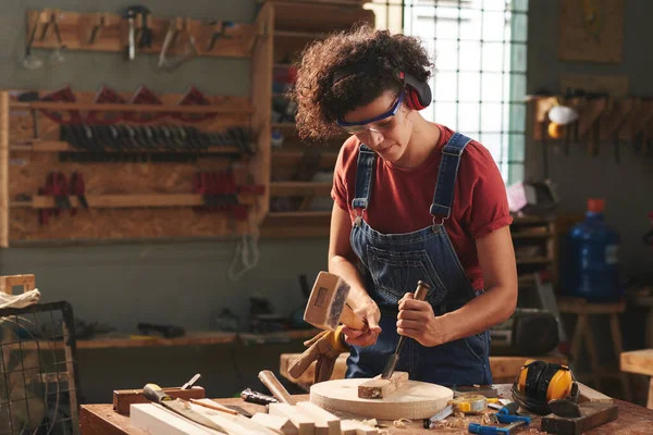 ワークショップで大工 木製の板で作業しながら ハンマーとチゼルを使用して耳の守備とゴーグルの集中巻き女性 — ストック写真