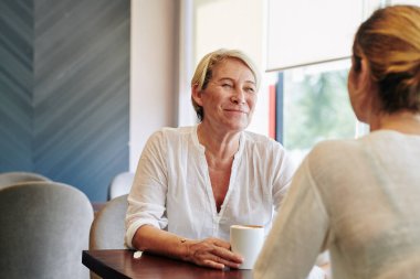 Gülümseyen olgun bir kadın yetişkin kızına bakıyor ve kafede buluştuklarında haber veriyor.