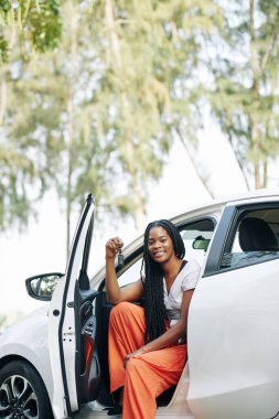 Mutlu güzel siyah kadın yeni arabasında oturuyor ve anahtarlarını gösteriyor.