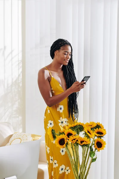 穿着黄色长裙 开着花的年轻貌美的女人在电话里看短信 — 图库照片