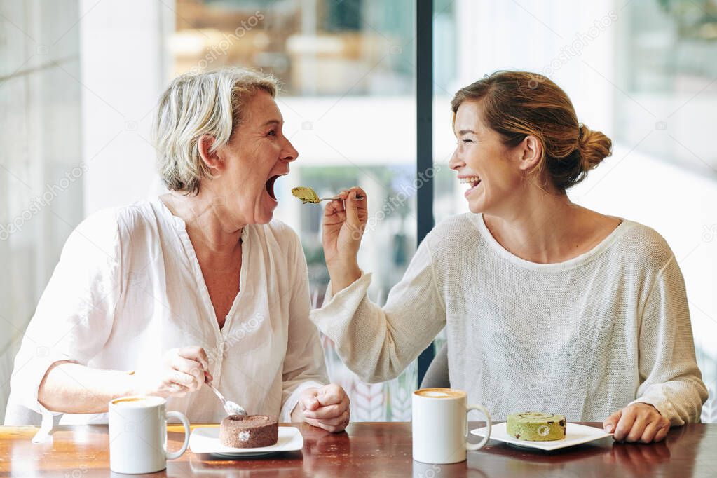 Happy pretty woman giving her mother a spoon of swiss roll she ordered for dessert