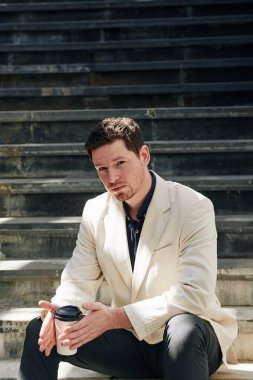 Genç yakışıklı bir adamın portresi basamaklarda dinleniyor ve kahve içiyor.