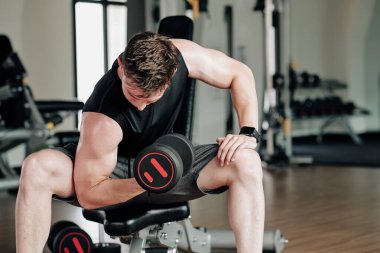 Formda bir genç adam spor yapıyor ve bisepsler için egzersiz yapıyor.