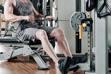 Formda bir adamın sıkı antrenman yaptığı ve kablo sıra makinesinde ağırlık çektiği görüntüler.