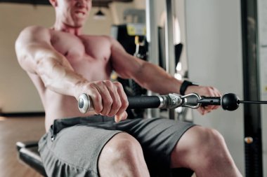 Güçlü kaslı genç adam ağır ağırlıklarla kürek çekme makinesinde egzersiz yapıyor.