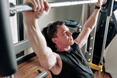 Jimnastik masasında otururken halter kaldıran azimli genç vücut geliştirici.