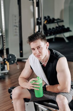 Yakışıklı, formda adam antrenmandan sonra bankta dinleniyor ve protein içeceği içiyor.
