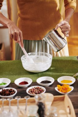 Büyük cam kasede sıvı sabun malzemelerini karıştıran bir kadın resmi.