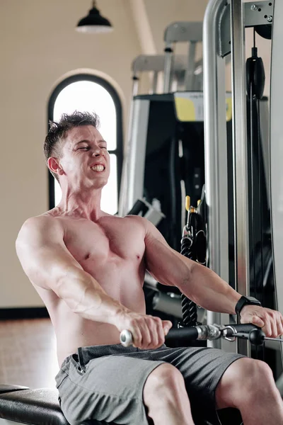 Kürek çekme makinesinde egzersiz yapan genç ve güçlü bir adam.