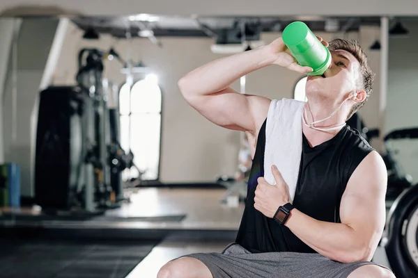 口渴的年轻健美运动员在健身房训练后喝维生素水 — 图库照片