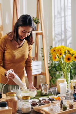 Evde sabun yaparken elektrikli mikser kullanan Vietnamlı genç bir kadın.