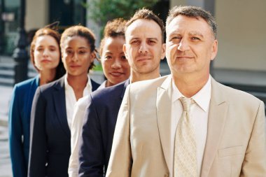 Olgun gülümseyen girişimci iş adamlarının önünde duruyor.