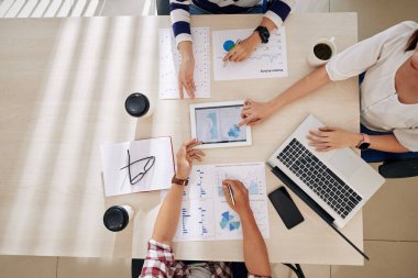 İş adamları büyük ofis masasında oturup mali belgeler ve raporlarla çalışırken iş ve şirket geliştirme yöntemlerini tartışırlar.