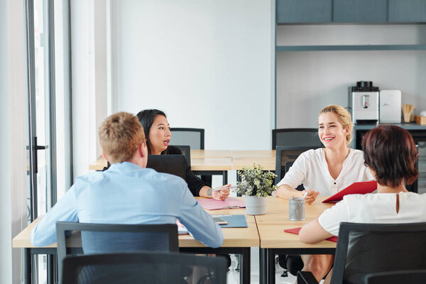 Группа молодых руководителей бизнеса, сидящих за большим офисным столом и обсуждающих развитие нового стартап-проекта