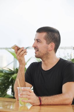 Yakışıklı genç adam ferahlatıcı narenciye içkisi içip sesli mesaj kaydediyor.