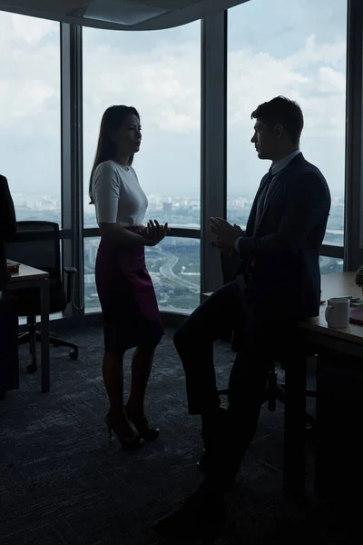 Business people having serious conversation in dark office with big panoramic windows