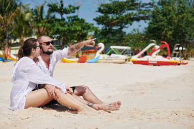 Genç adam denizi gösteriyor ve kız arkadaşına ilginç bir şey gösteriyor.