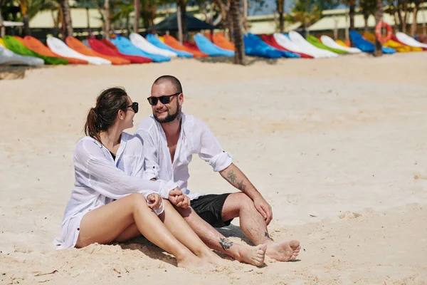 一对快乐的年轻夫妇坐在沙滩上讨论周末的计划 — 图库照片