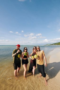 Tropik ada sahillerinde yürürken hindistan cevizi kokteyli içen bir grup mutlu arkadaş.