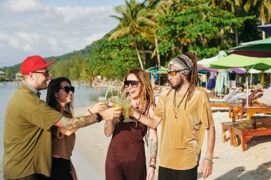 Neşeli arkadaşlar plaj partisinin tadını çıkarıyor ve bir bardak lezzetli kokteylle kadeh kaldırıyorlar.