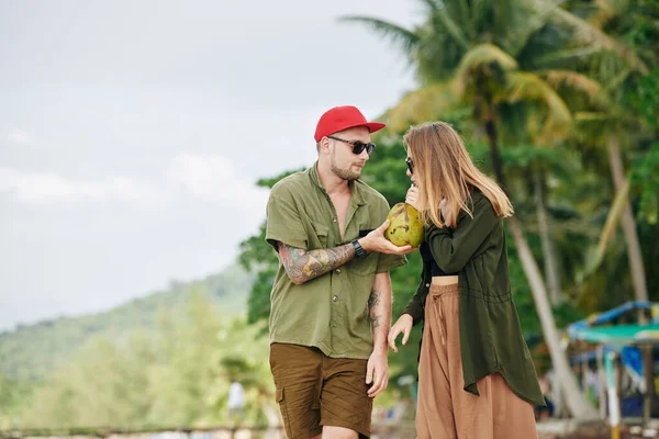 小伙子在海滩散步时 给了女友新鲜的椰子酱和吸管 — 图库照片