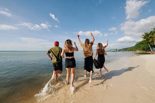 Joyful young people running in water on the beach, view from the beach