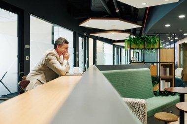 Stresli iş adamı, internette şok edici haberleri okurken elleri ile ağzını kapatıyor.