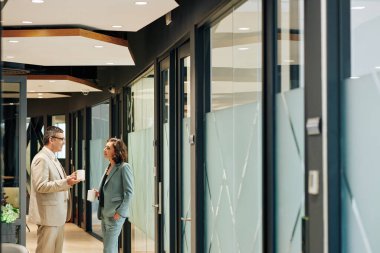 Gülümseyen işletme yöneticileri kahve içip modern ofis koridorlarında yeni projeler hakkında konuşuyorlar.