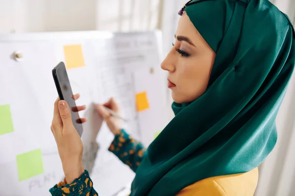Krásný Muslim Projektový Manažer Kontrolující Data Obrazovce Smartphonu Při Psaní — Stock fotografie