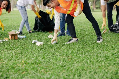 Parkta çöp toplarken parlak yelek ve lastik eldiven giyen genç gönüllüler