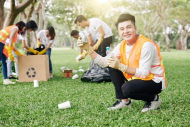 Şehir parkından topladığı teneke ve plastik şişeyi gösteren neşeli Vietnamlı gönüllü.