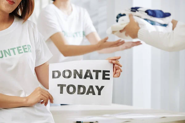 Cropped image of female volunteer holding donate today placard, man donating clothes in background