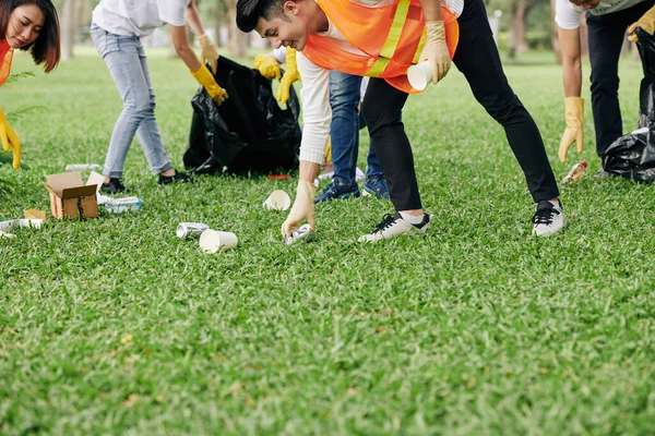 在公园收集垃圾时 年轻的义工穿着鲜艳的背心和橡胶手套 — 图库照片