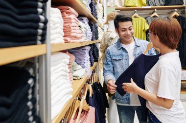 Yakışıklı Asyalı genç adama sıradan tişörtler seçmesinde yardımcı oluyor.