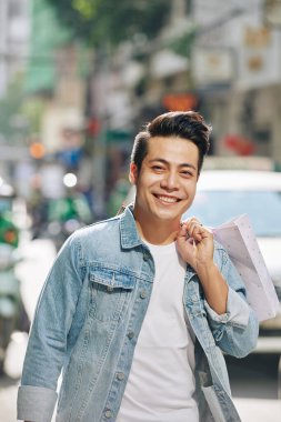 Genç yakışıklı Vietnamlı bir adamın portresi. Elinde alışveriş çantalarıyla dışarıda yürüyor.