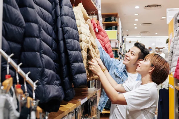 正の若いアジアのカップルのために達する暖かい冬のジャケットのためにハンガーで店 — ストック写真