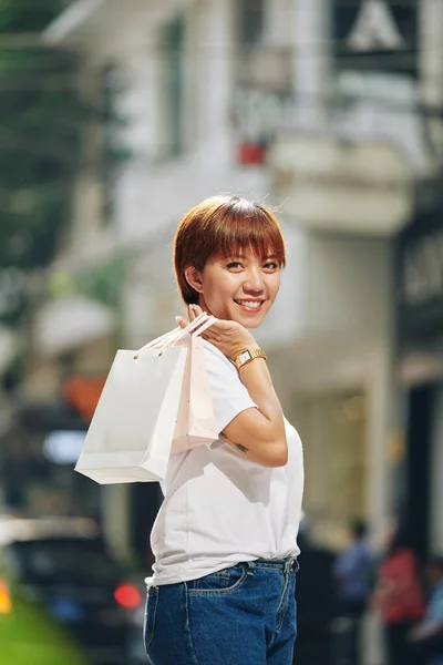 買い物の時間を過ごした後 手提げ袋を手に通りに立ってカジュアルな服を着た幸せな若いアジアの女性 — ストック写真