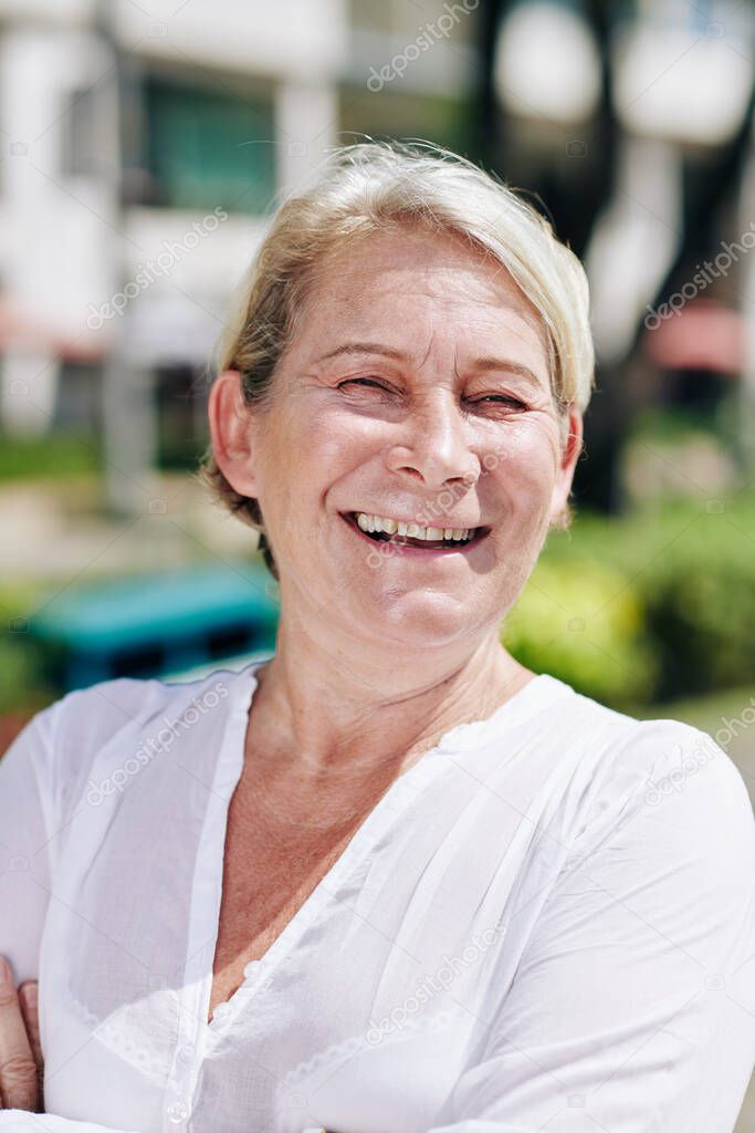 Portrait of laughing senior woman in white cotton blouse spending sunny day outdoors