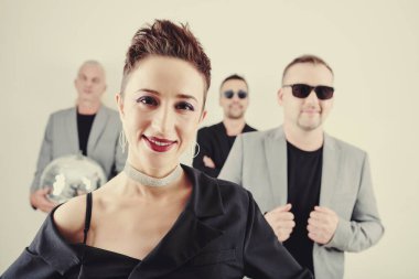 Güzel gülümseyen genç bir kadın müzik grubunun önünde duruyor.