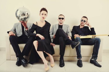 Konser kıyafetleri içinde şık yaratıcı müzik grubu kanepede gitar ve disko topuyla oturuyor.
