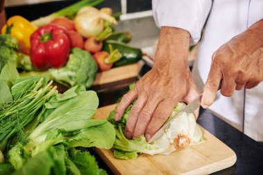 Tahtada keskin bir bıçakla marul kökünü kesen kıdemli bir adamın elleri.