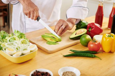 Akşam yemeği için bir kase lezzetli salata yaparken taze olgun avokado kesen aşçı.