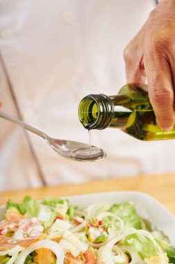 Salata kasesine bir kaşık sebze yağı döken adamın yakın plan görüntüsü.