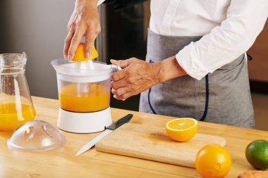 Olgun bir adam organik portakalların suyunu mutfak masasındaki plastik sıkacağıyla sıkıyor.