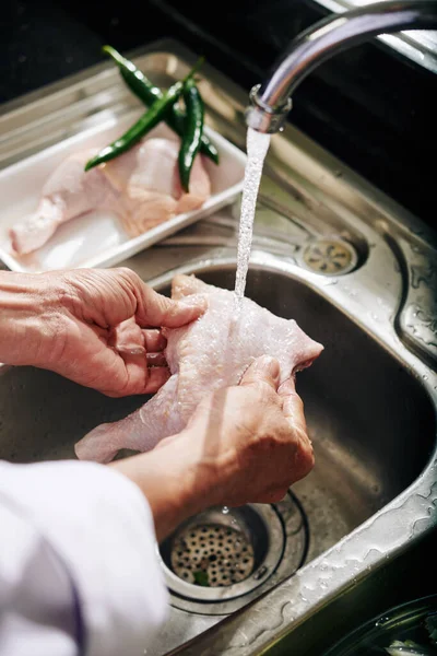 台所の蛇口から冷たい水の下で鶏をすすいでいる上級者の手 — ストック写真