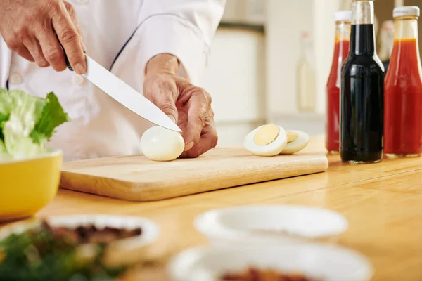 調理場でサラダを作るときに茹でた鶏の卵を切る料理人の手 — ストック写真